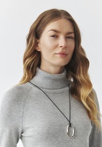 Gray knit turtleneck sweater, featuring ribbed texture. A long black cord necklace with a glossy silver oval pendant.
