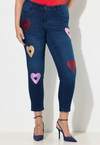 Tmavě modré džíny z denimu s krátkými nohavicemi, na přední straně zdobené barevnými vyšívanými srdcovými tvary v červené, růžové a zlaté barvě.