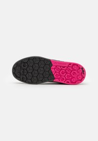 Semelle de chaussure en caoutchouc noire et rose avec un motif de crête hexagonale. Le talon présente une section rose texturée et le logo 'VAUDE'.