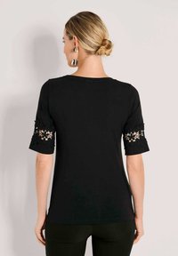 Black short-sleeve top featuring lace accents on sleeves, smooth texture, round neckline, and a fitted shape. Back view shown.