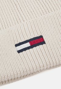 Gorro de punto en color crema con textura acanalada. Presenta una franja con logotipo bordado en rojo, blanco y marino en el puño doblado.