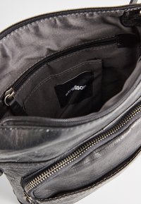 Interior de bolsa de cuero negro con una textura suave, que presenta un bolsillo con cremallera y una etiqueta con el logo. Forrada con tela oscura.