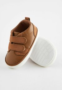 Scarpe per bambini in pelle marrone con due cinturini in Velcro, suole in gomma bianca, punta arrotondata e dettagli superficiali testurizzati.