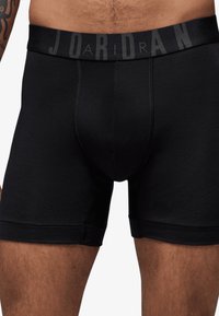 Boxers noirs avec une ceinture élastique douce arborant le texte "JORDAN" en imprimé sombre. Tissu lisse avec un design ajusté.