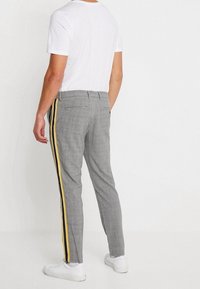 Šedé kostkované kalhoty s úzkým střihem, s žlutými bočními pruhy, nošené s jednobílým tričkem a bílými teniskami.