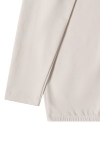 Hellbeige langärmliges Oberteil aus weichem Stoff. Mit abgerundetem Saum und Nahtdetails an den Bündchen und am unteren Saum. Glatte Textur.