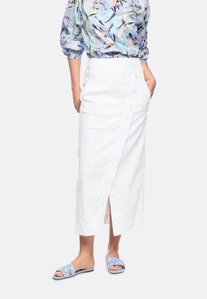 Woman wearing a white buttoned midi skirt, floral blouse with puffed sleeves, and light blue open-toe slide sandals.
