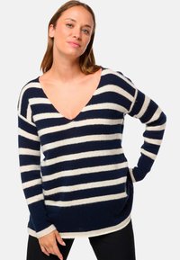Pull en tricot rayé bleu marine et crème, présentant un décolleté en V profond, des manches longues et une coupe décontractée avec un ourlet arrière légèrement plus long.
