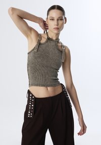 Top corto grigio a coste con collo all'americana e dettagli con cinturini. Pantaloni marroni con tasche laterali borchiate. Tessuto liscio con design aderente.