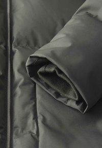 Giubbotto piumino grigio scuro, con un esterno liscio, zip completa e polsini a maglia verde scuro arrotolati che spuntano dalla manica.