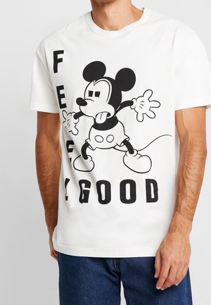 Homme portant un t-shirt blanc avec un dessin animé de souris noire et le texte en gras « FEELING GOOD » partiellement visible autour du personnage.