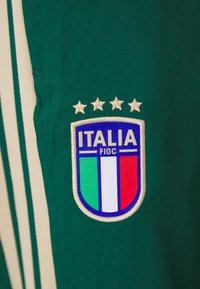 Πράσινη αθλητική φανέλα με το σήμα της ποδοσφαιρικής ομάδας της Ιταλίας, που διαθέτει τέσσερις αστέρες από πάνω και κατακόρυφες πράσινες, λευκές και κόκκινες ρίγες από κάτω.