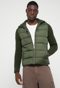 Roheline pehme vest rib-kootud varrukatega, lukuga kinnitamine ja seisma krae. Esipind on sile ning varrukatel on kootud detailid.