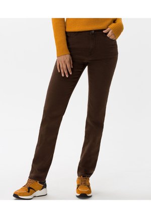 Persoon draagt een slimfit donkere bruine broek, mosterdgele trui en bijpassende mosterdgele sneakers met zwarte en witte zolen.