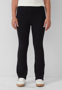 Zwarte stretchy broek met een aansluitend ontwerp, taps toelopende pijpen en een soepele textuur, gecombineerd met witte sneakers met een tan zool.