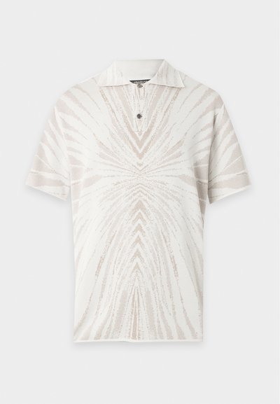 Polo blanc à manches courtes avec motif abstrait de rayures rayonnantes beige clair et un seul bouton noir sous le col.