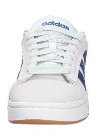 Sneaker bianco in suede con strisce blu, lacci piatti, linguetta imbottita e suola in gomma testurizzata. Nome del marchio "adidas" in blu sulla linguetta.