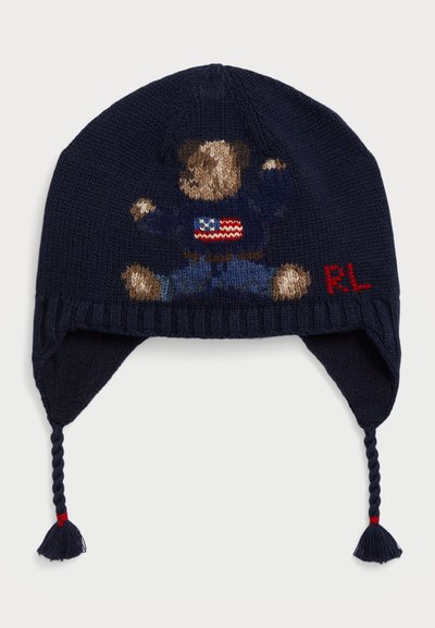 Cappello lavorato a maglia navy con grafica di orso, caratterizzato da legature intrecciate con pon-pon e accenti rossi. Tessuto strutturato con motivi intricati.