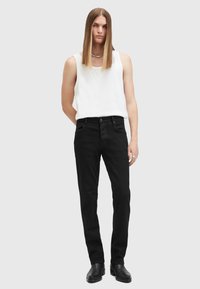 Vaqueros negros de corte ajustado y diseño de cinco bolsillos, combinados con una camiseta sin mangas blanca. Textura suave, estilo minimalista, sin patrones visibles.