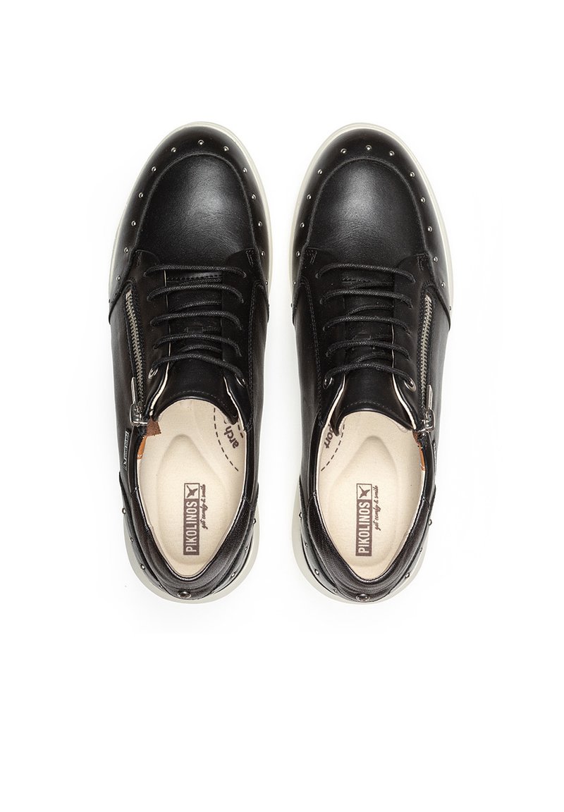 Zapatillas de cuero negro con punta redonda, tachuelas plateadas a lo largo de la suela, cierre de cremallera en el lateral y un interior beige en contraste.