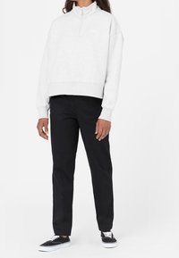 Ljusgrå fleece zip-up sweatshirt med hög krage, i kombination med svarta raka byxor och svarta sneakers med vita sulor.