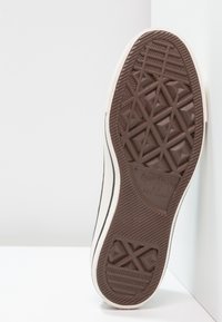 Semelle d'une basket Converse All Star blanche montrant une bande de roulement en caoutchouc marron avec un motif d'étoile et de losange.