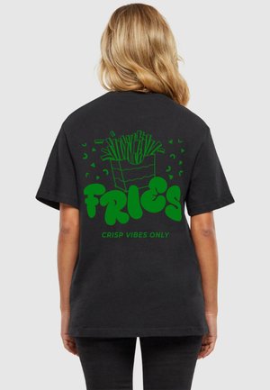 Fekete póló zöld grafikával, amelyen egy sültkrumpli doboz látható, alatta a "FRIES" és a "CRISP VIBES ONLY" felirattal.