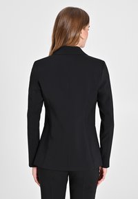 Blazer nero su misura con una silhouette strutturata, rever a notched e maniche lunghe. Tessuto liscio e design aderente, che enfatizza una forma snella.