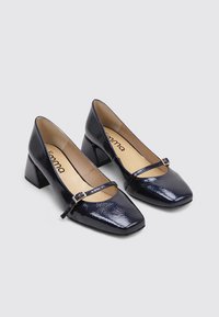 Chaussures à talons blocs en cuir verni bleu marine avec un bout carré, comportant une fine sangle et une boucle en métal sur le cou-de-pied.