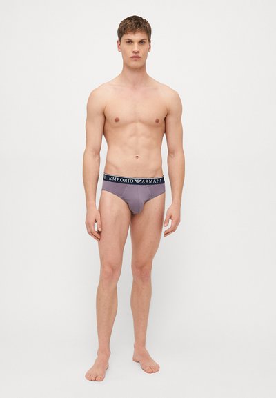 Caleçons gris avec une ceinture marine portant le logo "Emporio Armani", design ajusté, tissu doux et coupe basse, portés par un mannequin masculin.