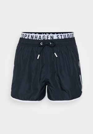 Pantaloni de baie negri cu șnur și talie albă, având textul "Copenhagen Studios"; includ accente laterale albe. Material neted.