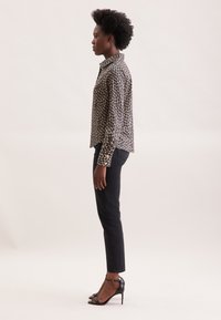 Camicia a maniche lunghe con stampa leopardata in beige e nero, abbinata a jeans neri attillati e sandali neri con tacco alto. Vista laterale.