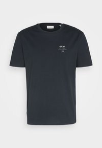 T-shirt bleu marine en coton. Présente un col rond, des manches courtes et un imprimé blanc du logo GANT sur la poitrine gauche.