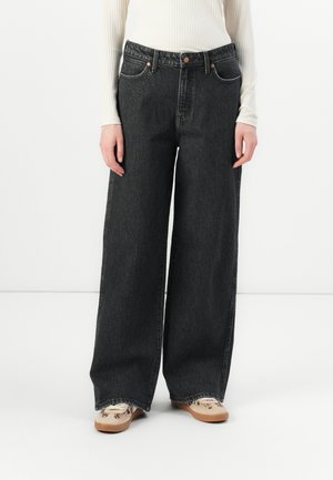 Vide ben svarte denimbukser med høy midje, med mørk søm og frontlommer. Kombinert med mønstrede beige sko.