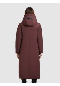 Hosszú bordó puffermellény nagy kapucnival, háton logó folttal, sima textúrával és oldalsó szellőzőkkel a mozgás érdekében.