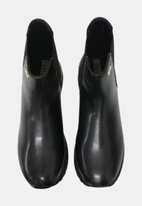 Stivaletti neri alla caviglia realizzati in pelle lucida con una texture liscia, dotati di pannelli laterali elastici e design con punta arrotondata. Dettagli in oro presenti.