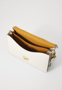 White leather clutch bag with a gold oval clasp, opened to reveal a golden interior and a small brown cardholder. Smooth texture, minimal design.