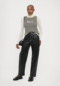Svart och vit rutigt ärmlöst linne över en långärmad krämfärgad turtleneck, kombinerat med lösa svarta läderbyxor och svarta skor.