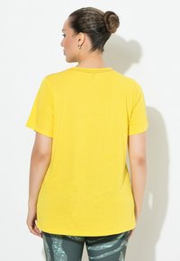 Maglietta gialla a maniche corte con vestibilità comoda e scollatura rotonda, abbinata a leggings verdi a fantasia. Tessuto liscio con una leggera lucentezza.
