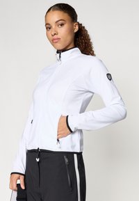 Valge tõmblukuga jakk, millel on kõrge krae, must tõmblukk ja küljetaskud. Mustad aktsendid mansettidel ja allääres. Pehme ja sile tekstuur.