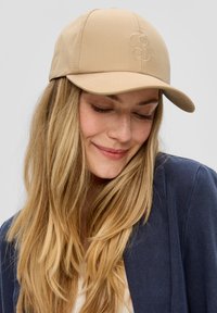 Beige pet van gladde stof met een gestikt logo aan de voorkant, voorzien van een gebogen klep en een aansluitend ontwerp.