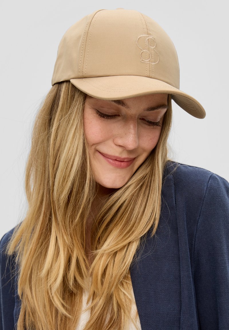 Beige pet van gladde stof met een gestikt logo aan de voorkant, voorzien van een gebogen klep en een aansluitend ontwerp.