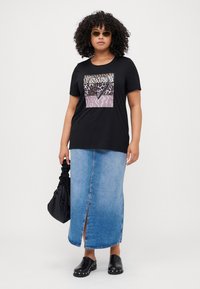 Schwarzes T-Shirt mit Tierdruckdesign, Jeans-Midi-Rock, schwarze Slipper und eine schwarze geraffte Handtasche. Das Model trägt Sonnenbrillen.