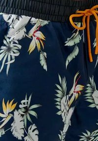 Shorts de bain à motifs floraux avec un fond bleu foncé et des motifs de feuilles et de fleurs tropicales. Comprend une taille élastique et un cordon de serrage orange.