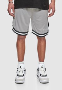 Shorts de basketball gris avec des rayures noires, présentant une texture en maille et un logo brodé. Associés à des chaussures de sport blanches et noires.