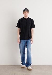 Svart t-skjorte med kort erme og rund hals, kombinert med lyseblå straight-leg jeans og hvite joggesko. Svart caps med hvit logo.