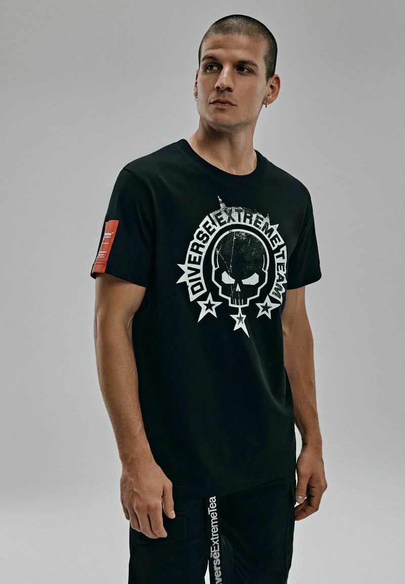 Czarna bawełniana koszulka z dużym białym wzorem czaszki i gwiazdkami. Posiada czerwoną metkę na lewym rękawie. Krótkie rękawy oraz okrągły dekolt.