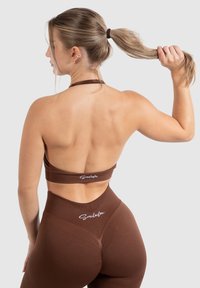 Top corto deportivo marrón y leggings de cintura alta hechos de tejido acanalado. Presenta un diseño de espalda con corte y acentos de logotipo. Textura suave.