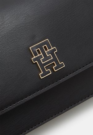 Sort læder crossbody-taske med gulddetaljer, med klaplukning og en guldfarvet logoemblem foran.