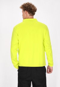 Suéter de manga larga en amarillo brillante, con cuello tipo polo, textura suave y un diseño ajustado, combinado con pantalones negros.